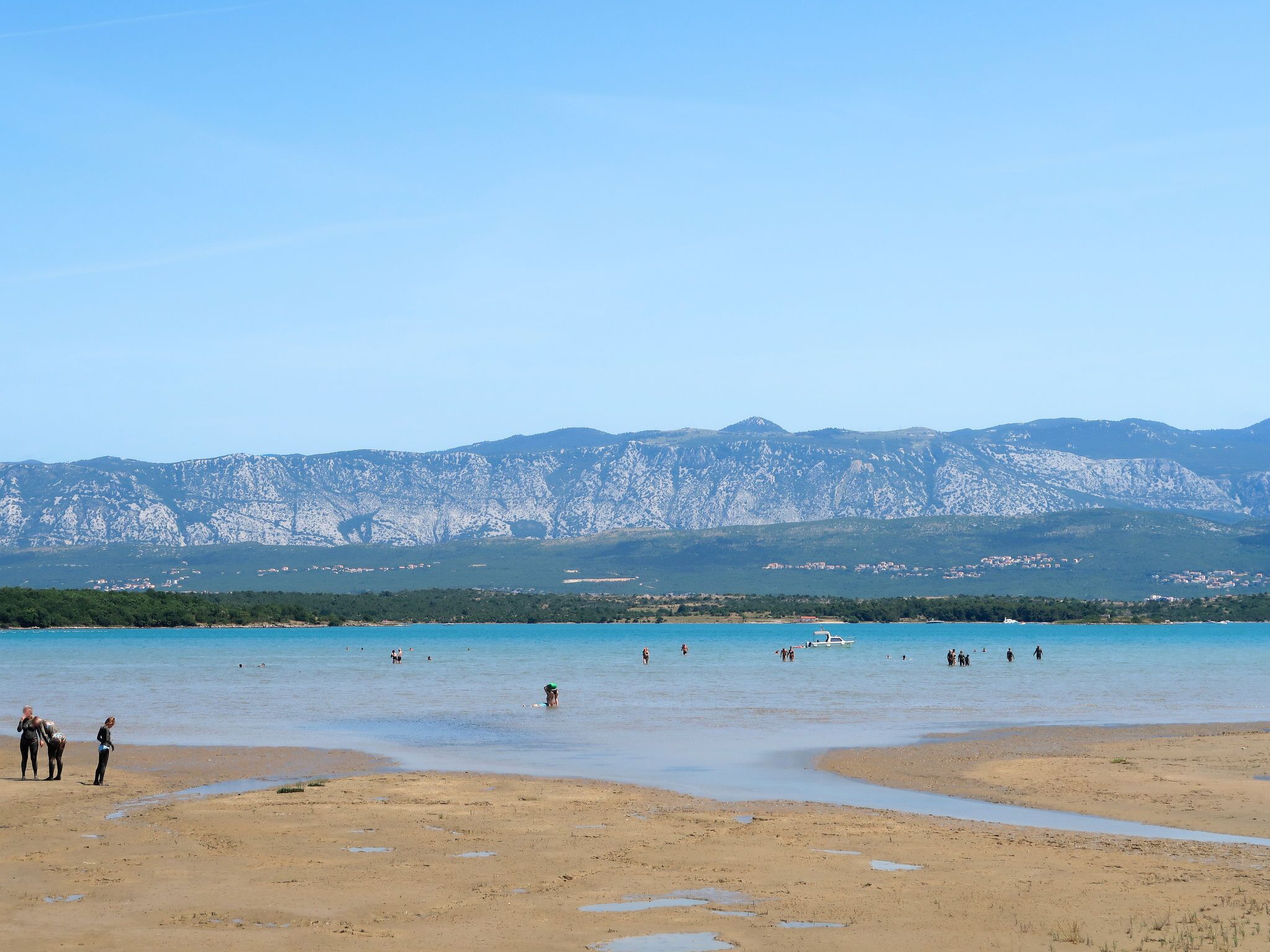 A beach with people and a boat, mountains in the background, and a clear sky.