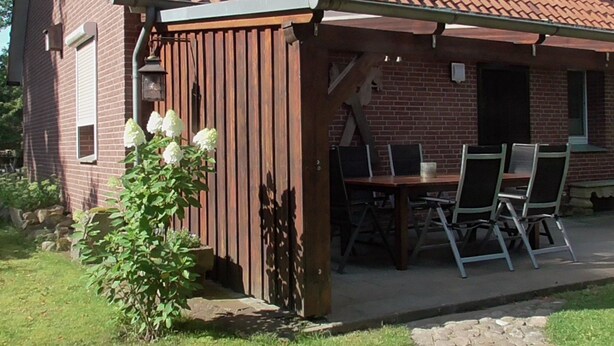 A covered patio with a brick house, a wooden table, and chairs. - mit überdachter Terrasse und Carport by Interhome (Walsrode)