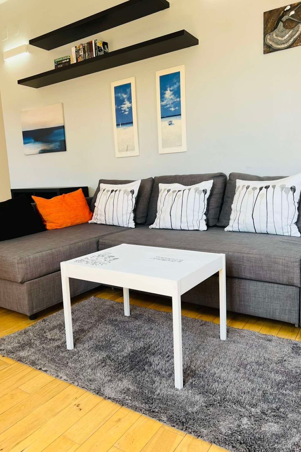 A modern living room with a grey sofa, white and striped pillows, a white coffee table, and a grey shag rug.