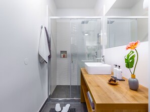 Un baño moderno con cabina de ducha de vidrio, tocador de madera con lavamanos y espejo.