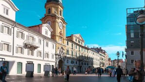 A spacious public square with historic buildings, a prominent clock tower, and a clear blue sky.