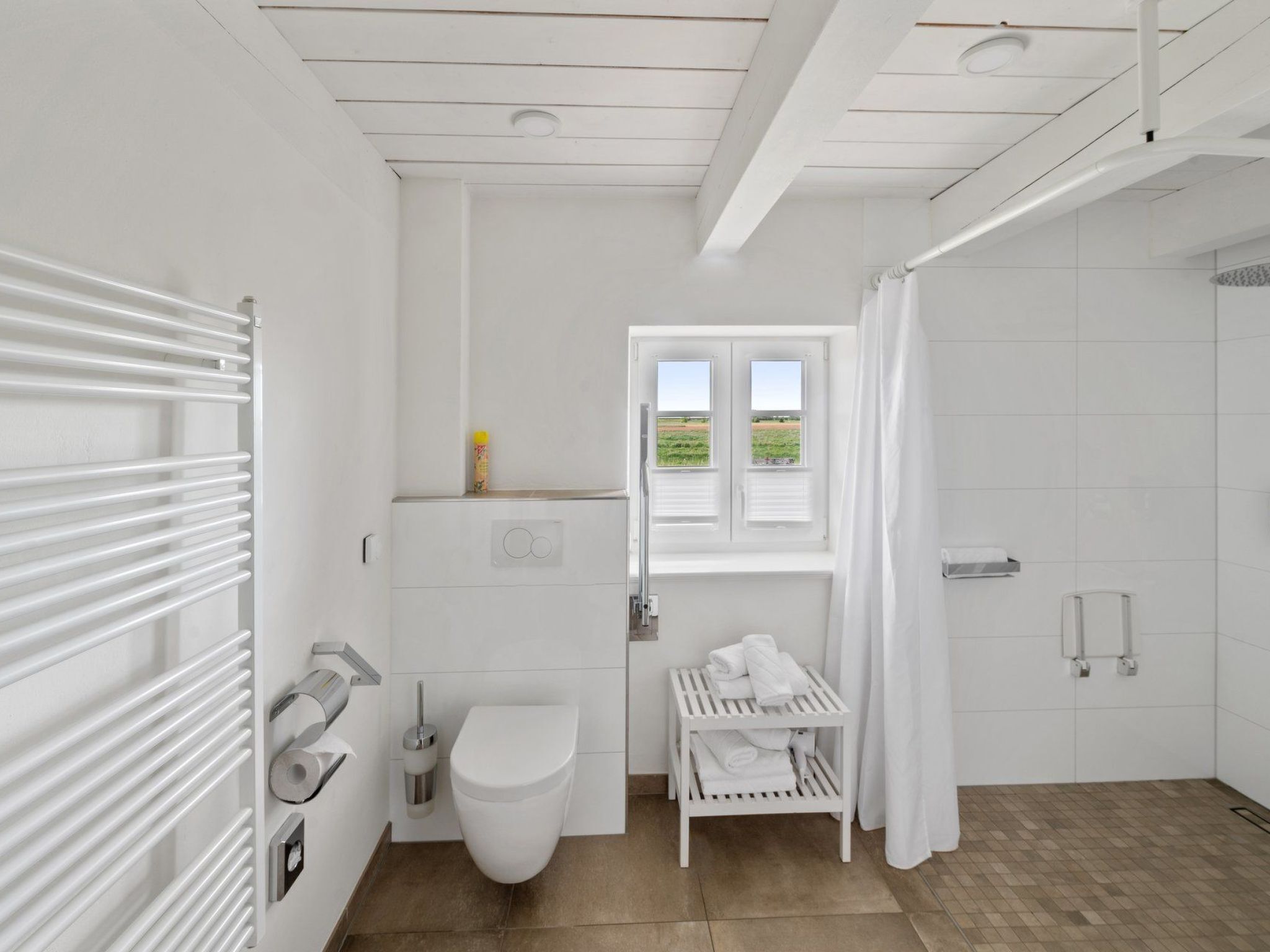 Et moderne badeværelse med toilet, bidet, håndklædeholder og et vindue med udsigt over et grønt område.