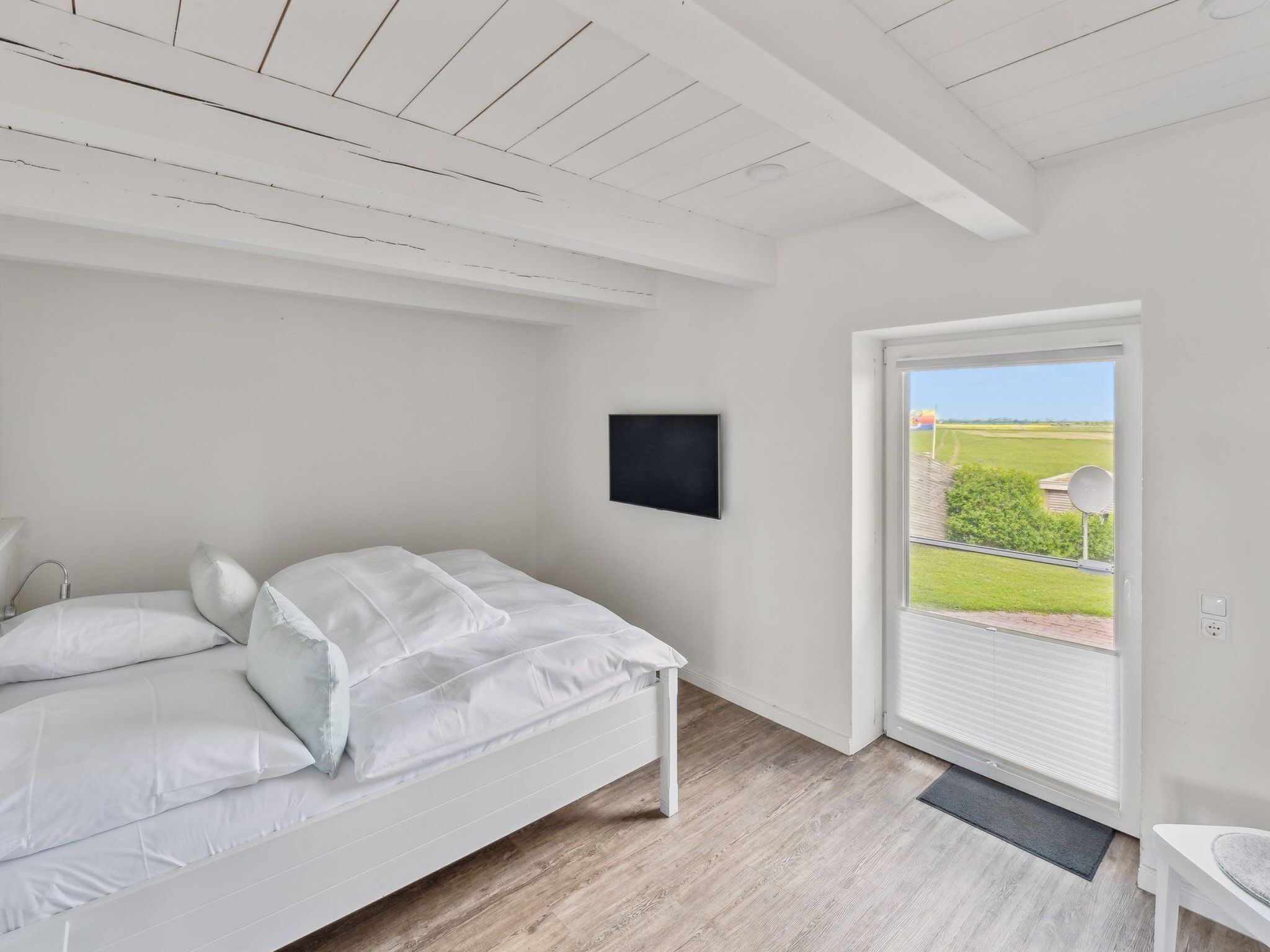 Ein Schlafzimmer mit Bett, kleinem Tisch, Fernseher und einer Tür zu einem Balkon mit Blick auf die Landschaft.