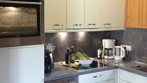 Een moderne keuken met witte kasten, een inbouwoven, een koffiezetapparaat en een waterkoker op het aanrecht.