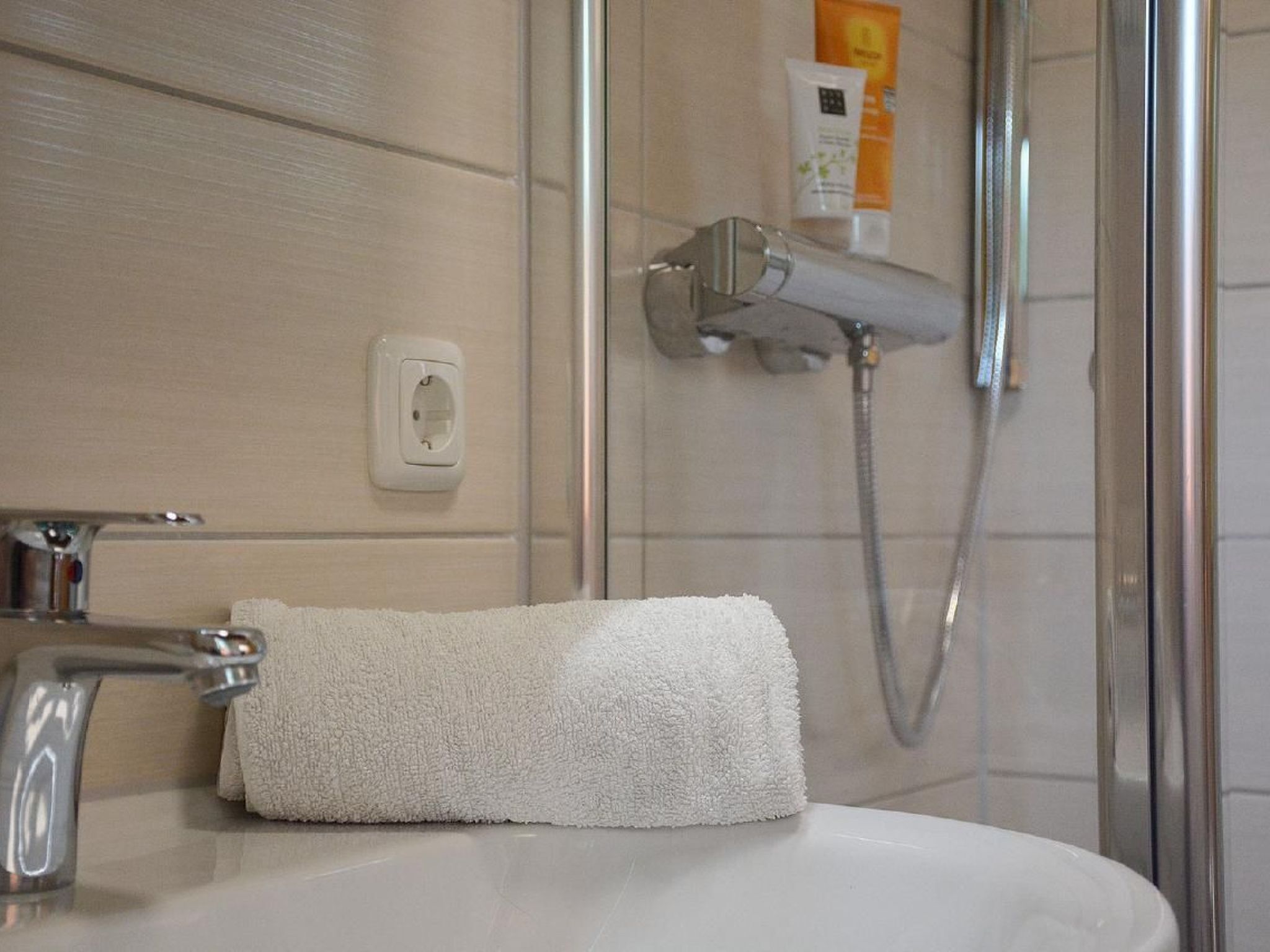Une salle de bain avec un lavabo blanc, une serviette, une pomme de douche et une paroi de douche en verre.