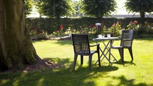 Un'area salotto esterna con tavolo e sedie, immersa in un giardino curato con alberi e fiori.