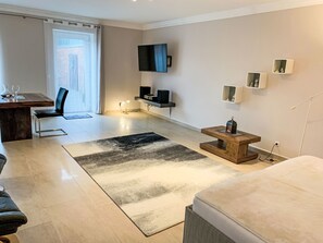 Een moderne woonkamer met een flatscreen televisie, een eethoek met tafel en stoelen, een salontafel en een bank.