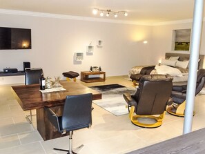 Een moderne woonkamer met een eethoek, een zithoek en een flatscreen televisie aan de muur.