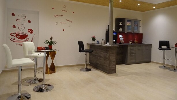 Un'area bar moderna con soffitto in legno, un'opera d'arte a tema caffè e una cucina sullo sfondo.