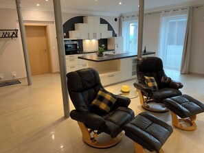 A modern living room with two reclining chairs, a small coffee table, and a kitchen in the background. - Modern eingerichtete Suite mit Terrasse by Interhome (Elskop)