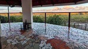 Une vaste terrasse ouverte, dotée d’un sol en mosaïque, de grandes fenêtres offrant une vue sur un paysage lointain et d’un espace détente extérieur simple.