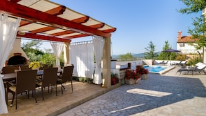 An outdoor patio with a brick table and chairs, a pool, and a pergola with white curtains. - "Villa Agneza" by Interhome (Pula/Rakalj)