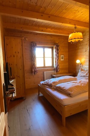 A wooden cabin bedroom with a bed, a window with curtains, a radiator, and a hanging lamp. - Berghütte mit Blick auf die Berge by Interhome (Rangersdorf)