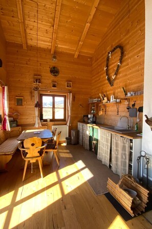 A cozy cabin interior with a wooden interior, a dining area with a table and chairs, a kitchen with a sink and cabinets, and a window providing natural light. - Berghütte mit Blick auf die Berge by Interhome (Rangersdorf)