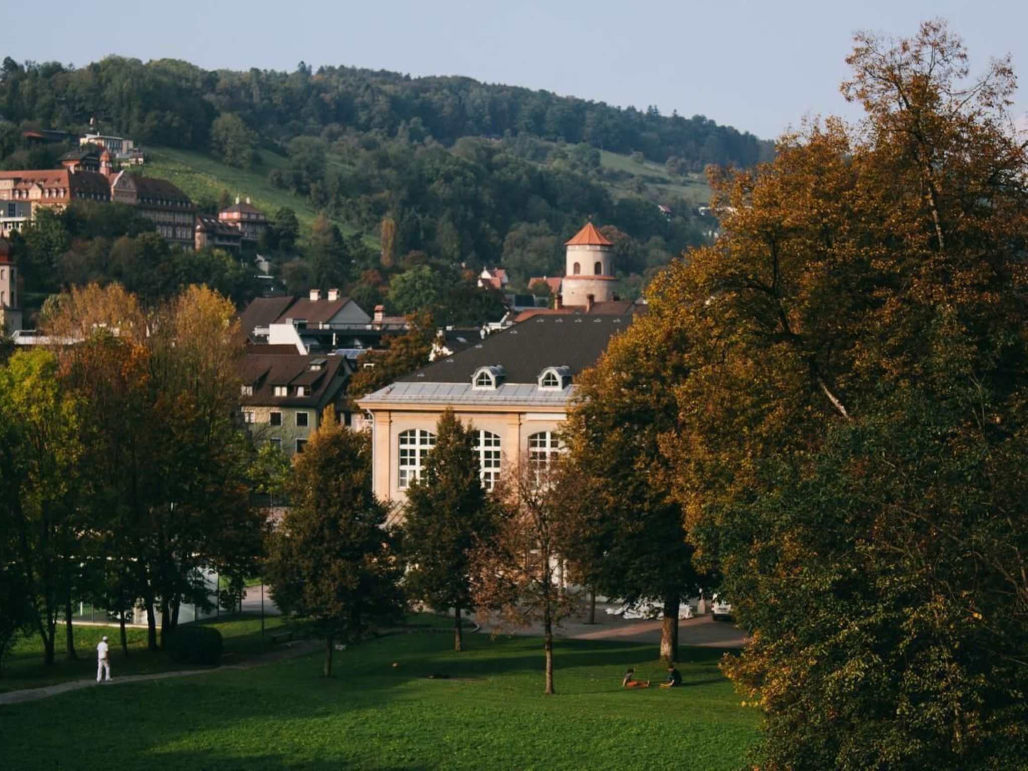 A park with a building in the foreground and a hill with houses in the background.