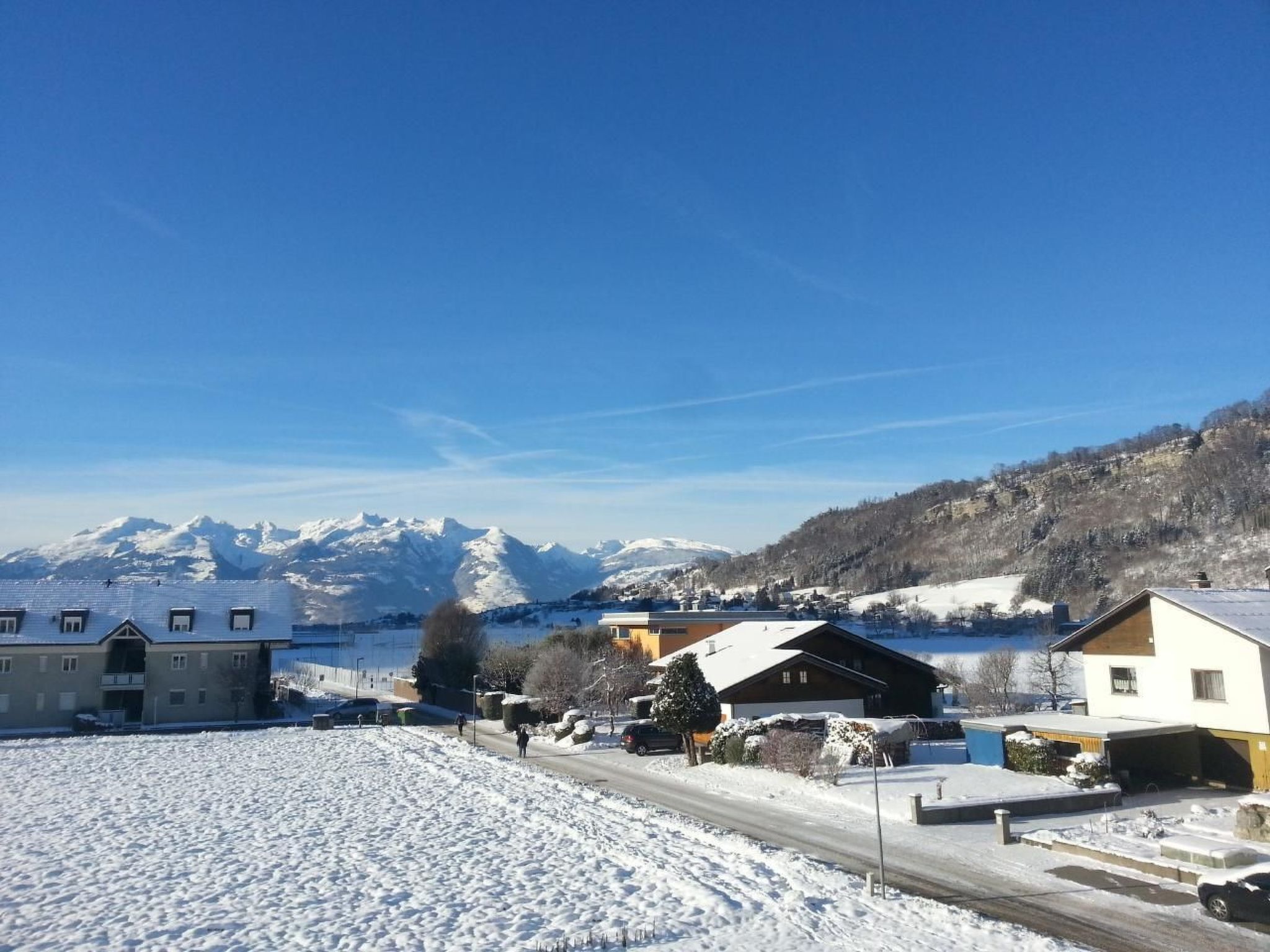 A snowy landscape with a road, buildings, and mountains in the background.