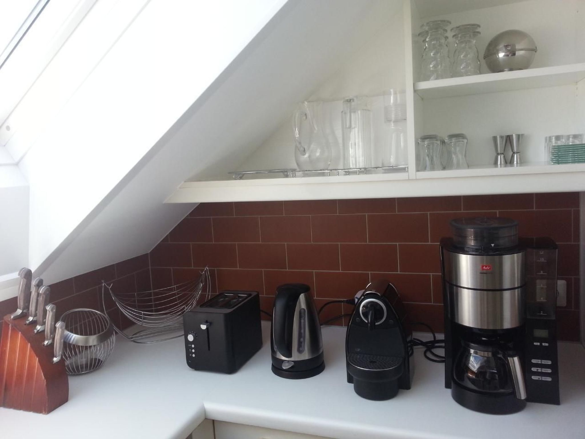 A kitchen with a white countertop, a coffee maker, a toaster, a kettle, and a blender.