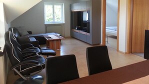 A modern living room with a sofa, chairs, a dining table, and a kitchen area with cabinets and a TV. - Apartement Feldkirch by Interhome (Feldkirch)