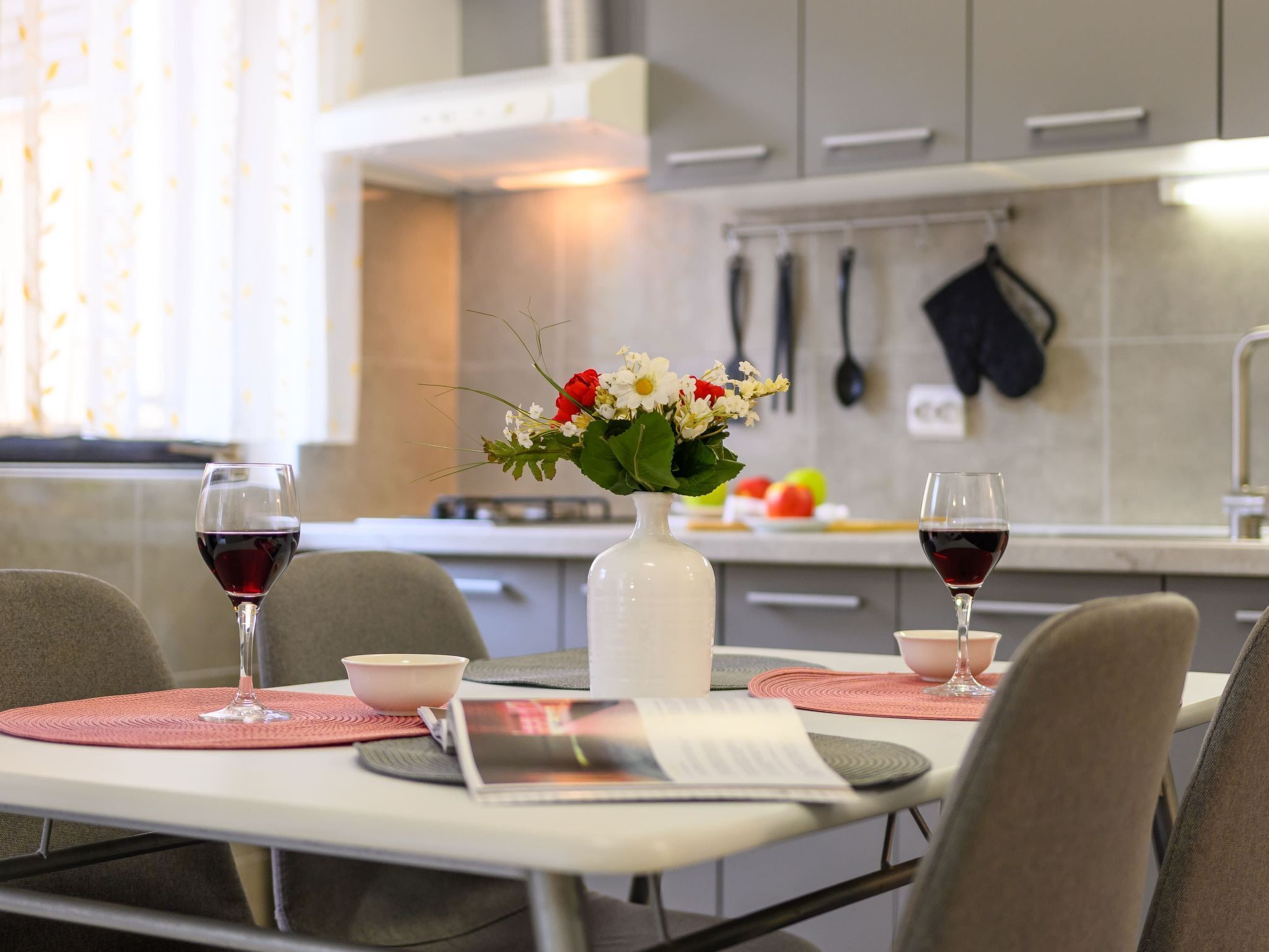 Una cocina moderna con una mesa de comedor para dos personas, con dos copas de vino y un florero con flores.