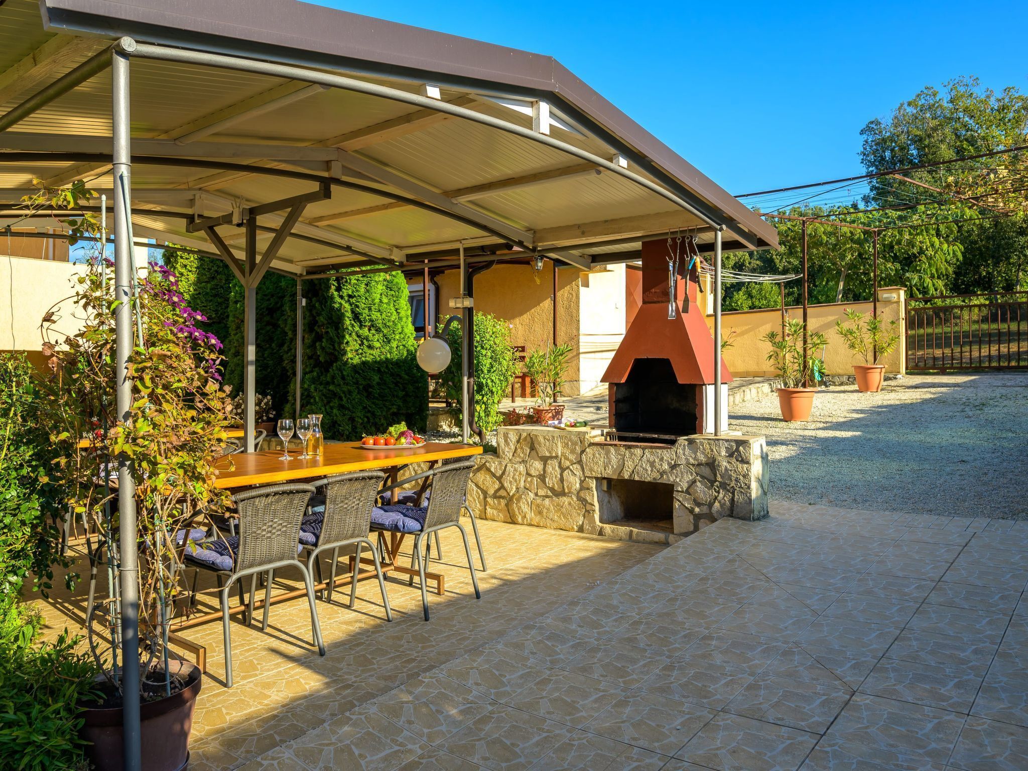An outdoor patio with a covered dining area, stone flooring, and a brick oven.