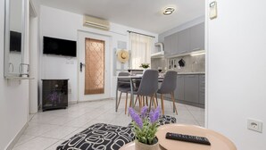 Une cuisine moderne avec des meubles gris, un coin repas comprenant une table et des chaises, et un téléviseur fixé au mur.