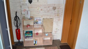 Quarto com parede de madeira, uma estante com livros e um aspirador de pó, porta com um número e uma decoração em formato de coração.