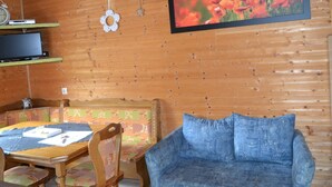 Um quarto aconchegante com decoração em madeira, uma televisão em uma estante, um quadro com flores e um sofá azul.