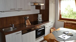 Uma cozinha compacta com lava-louças, forno e cafeteira. Há uma janela que oferece luz natural e vista para o verde lá fora.