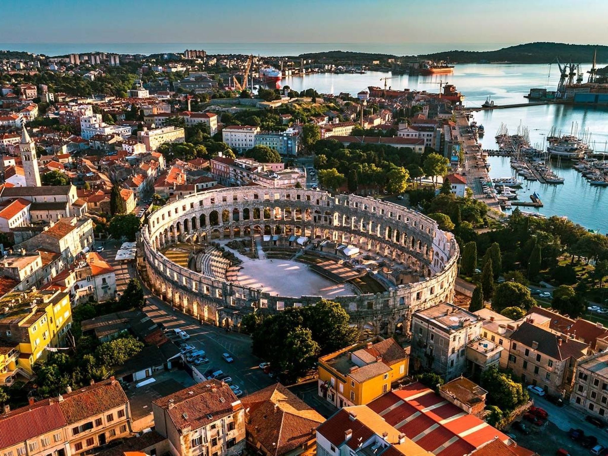 Un edificio storico circolare circondato da altri edifici urbani e un porto turistico.