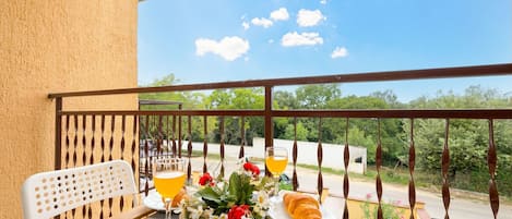 A balcony with a table set for breakfast, including croissants, flowers, and a glass of orange juice.