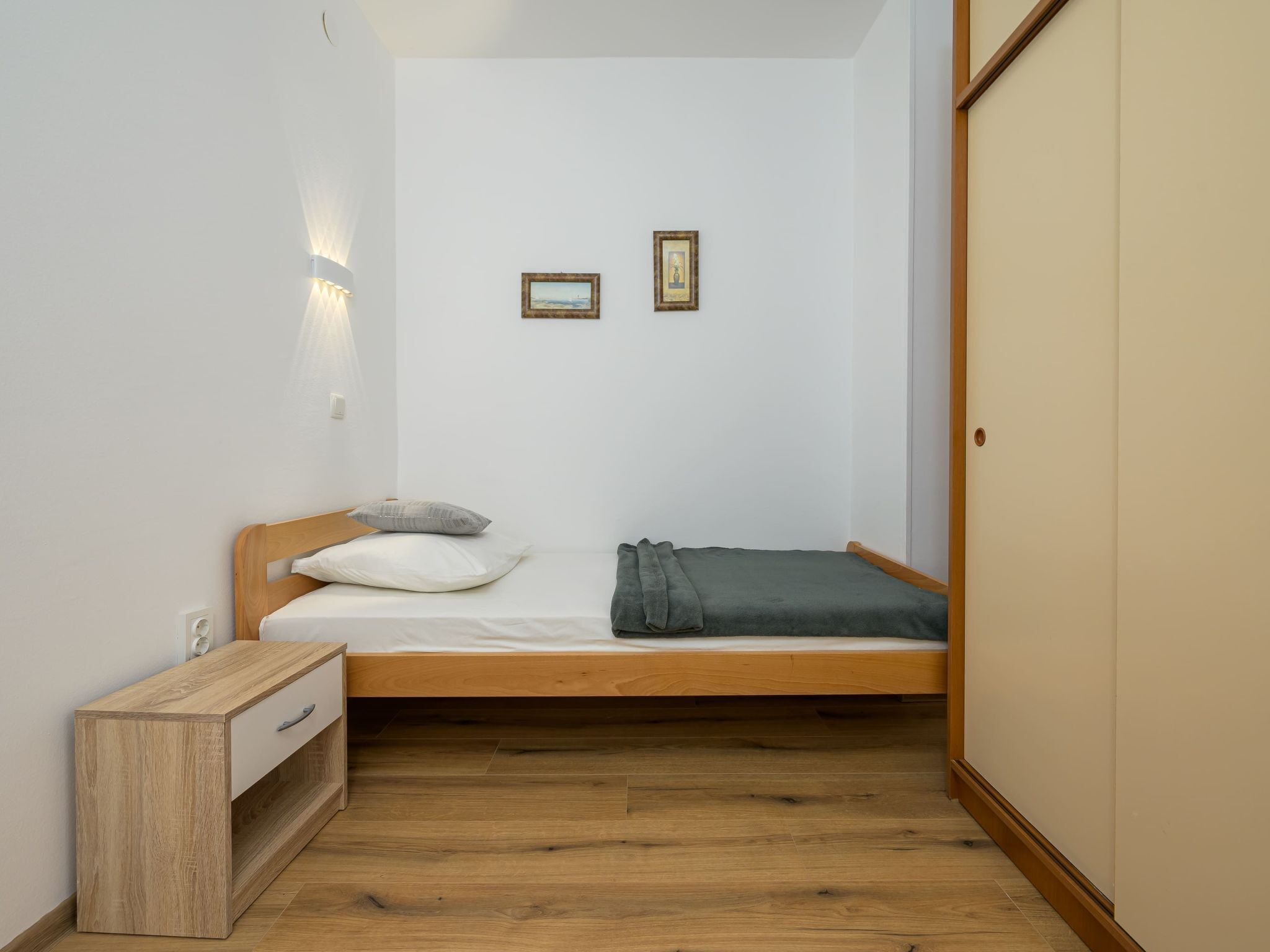 A small, single-bed room with a wooden headboard, a bedside table, and a wardrobe.