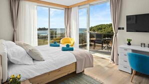A bedroom with a large bed, a balcony with a yellow chair, and a TV on the wall. - Villa Palma - Luxusvilla am Meer für 6 Personen by Interhome (Pula)