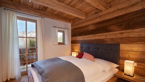 Ein Schlafzimmer einer Holzhütte mit einem großen Bett, einem Fenster mit Vorhängen und einem Nachttisch mit Lampe.