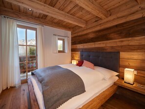 Ein Schlafzimmer einer Holzhütte mit einem großen Bett, einem Fenster mit Vorhängen und einem Nachttisch mit Lampe.