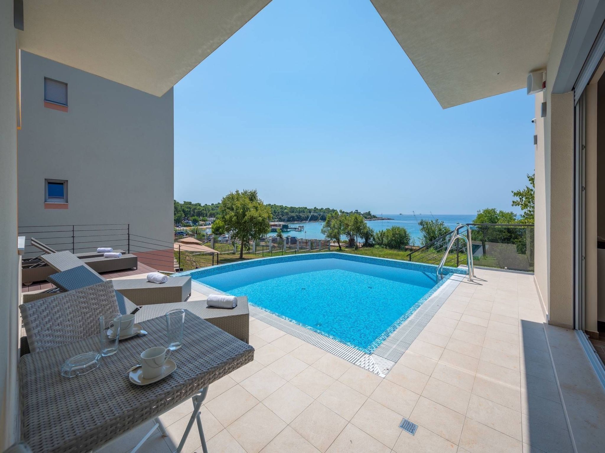 Ein Balkon mit Swimmingpool, Liegestühlen und einem Tisch mit Gläsern und Tassen.