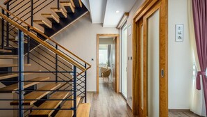 A modern interior with a wooden staircase, a hallway leading to a bathroom, and a door with a wooden frame. - Villa Magnolia by Interhome (Pula)