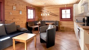 A cozy cabin-style room with a wooden interior, a sofa, a dining table, and a kitchen area.