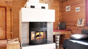 A cozy cabin interior with a stone fireplace, wooden walls, and a bench by the fireplace.