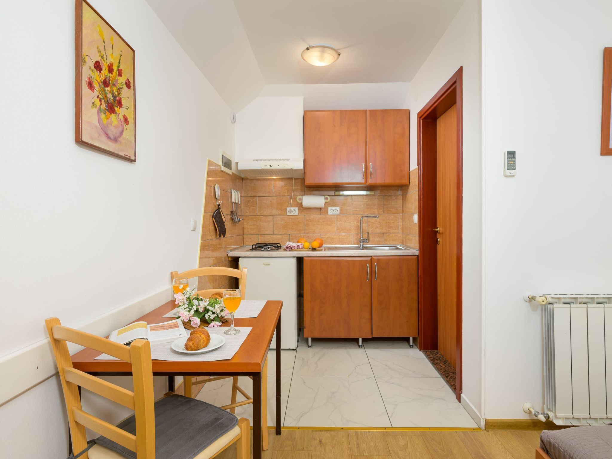 A compact kitchen with wooden cabinets, a small refrigerator, and a dining table with a chair.