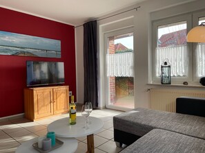 Ein Wohnzimmer mit roter Wand, einem Holzschrank, einem runden Tisch mit Flasche und Gläsern sowie einem grauen Sofa.