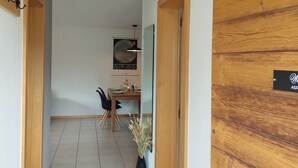 En hall med en trädörr, ett matområde med ett bord och stolar samt en väggmonterad lampa.