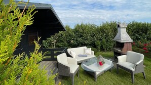 Eine Terrasse mit Korbmöbeln, einem Glastisch und einem Steinkamin.