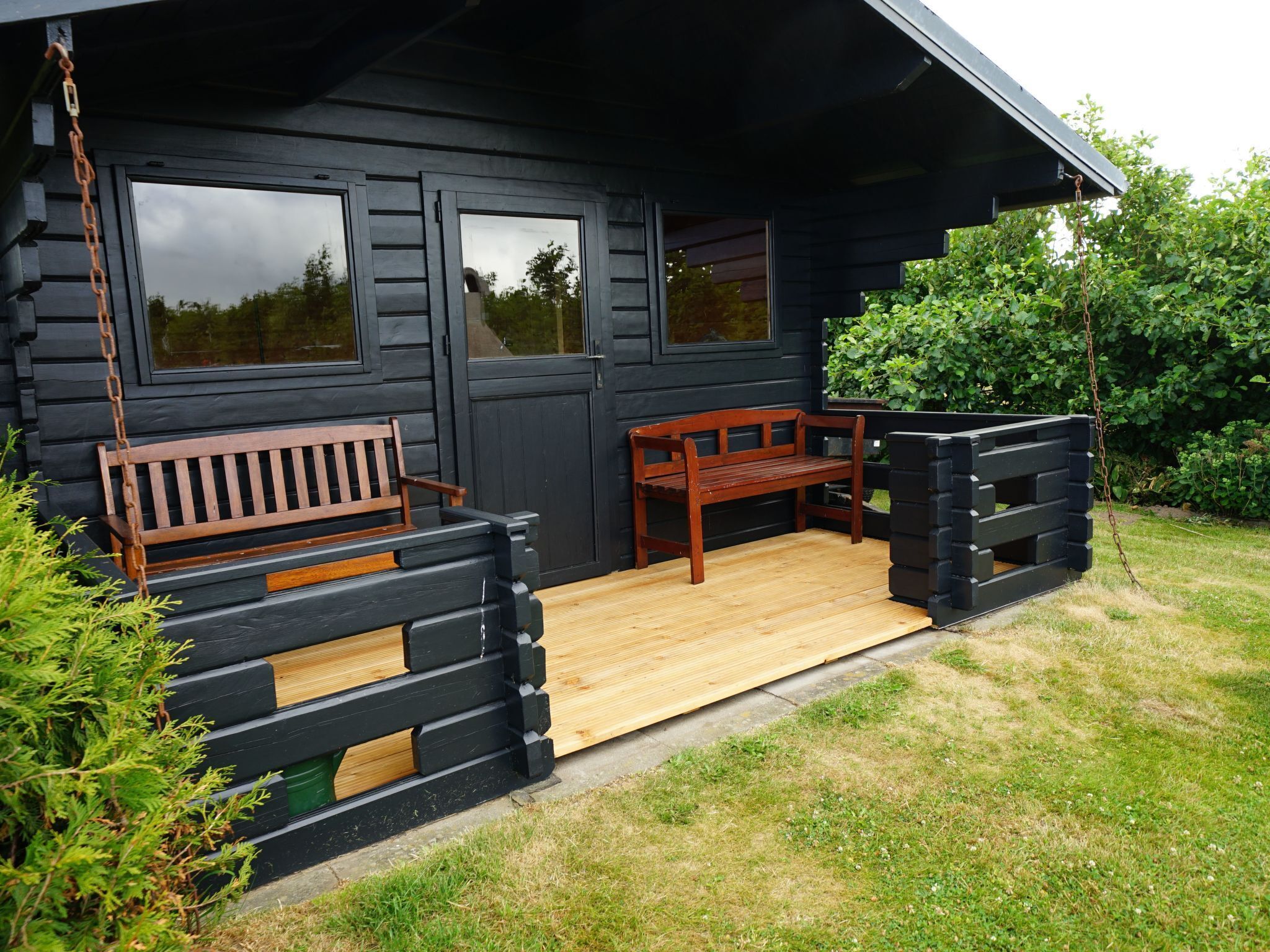 A wooden bench and a table outside a black wooden building with a porch.