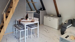 Ein kompakter, moderner Lofts Schlafbereich mit schrägen Wänden, einer kleinen Küchenzeile, einem Essbereich und einer Sitzecke.