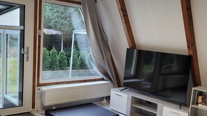 Ein modernes Wohnzimmer mit großem Fernseher, einer Couch und einem Fenster mit Blick auf einen Garten.