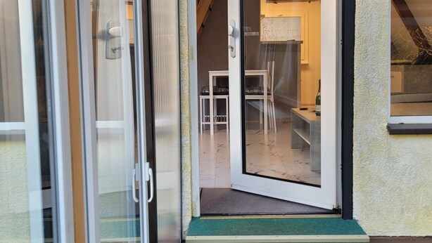 Ein moderner Gebäudeeingang mit Glastür, Holztreppe und einer kleinen Außenbereich-Sitzgelegenheit.
