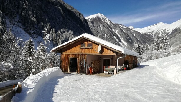 A wooden chalet with a snow-covered roof, situated in a snowy mountainous area with clear skies. - am Wallnerhof in Flattach by Interhome (Flattach)