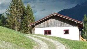A rustic wooden house with a white facade and red window frames, situated on a grassy hillside with a winding path leading to it. - am Wallnerhof in Flattach by Interhome (Flattach)