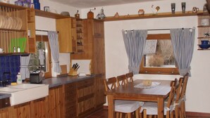 A kitchen with wooden cabinets, a dining table with chairs, and a window with curtains. - am Wallnerhof in Flattach by Interhome (Flattach)