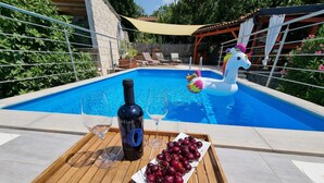 A wooden table with a bottle of wine, glasses, and a plate of cherries by a pool with a unicorn float. - mit privatem Pool und Sauna by Interhome (Crikvenica/Jadranovo)